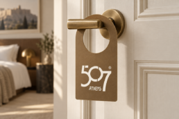 Bronze hotel door hanger with the 507 Athens logo on a brass door handle