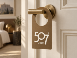 Bronze hotel door hanger with the 507 Athens logo on a brass door handle