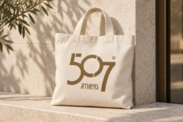 Ivory canvas tote bag with the bronze 507 Athens logo on a limestone bench