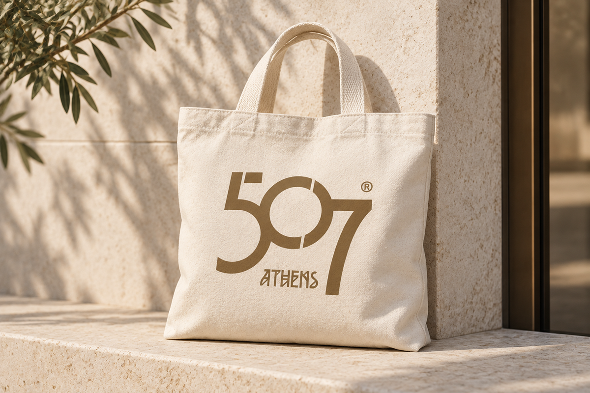 Ivory canvas tote bag with the bronze 507 Athens logo on a limestone bench