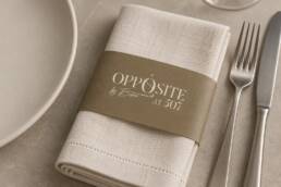 Ivory linen napkin mockup with a gold paper sleeve and the Opposite logo