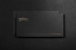 Charcoal envelope mockup with the Opposite by Botrini at 507 logo in gold foil