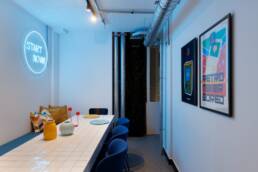 Retroverse posters and Start Now neon in a shared social space